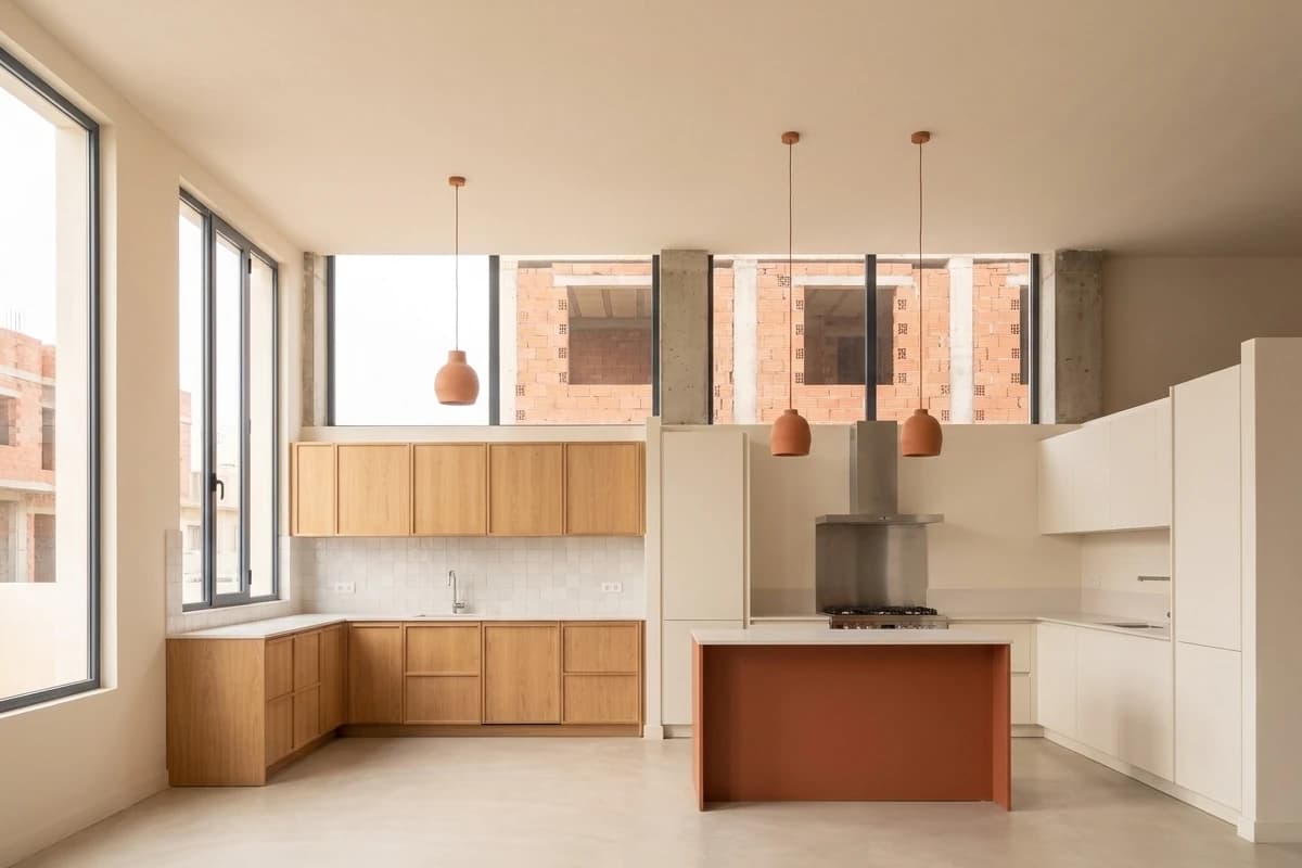 Deux cuisines d’exposition : chêne naturel et blanc mat avec un îlot terracotta.