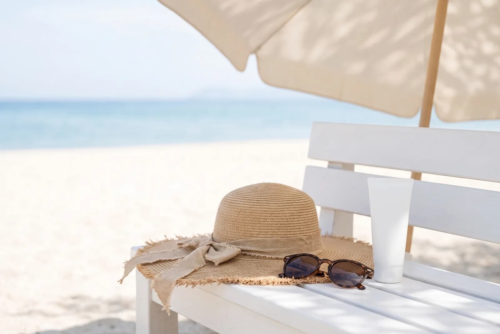 Un chapeau de paille et une serviette pliée à l’ombre d’un parasol, sur une plage calme en fin de matinée.