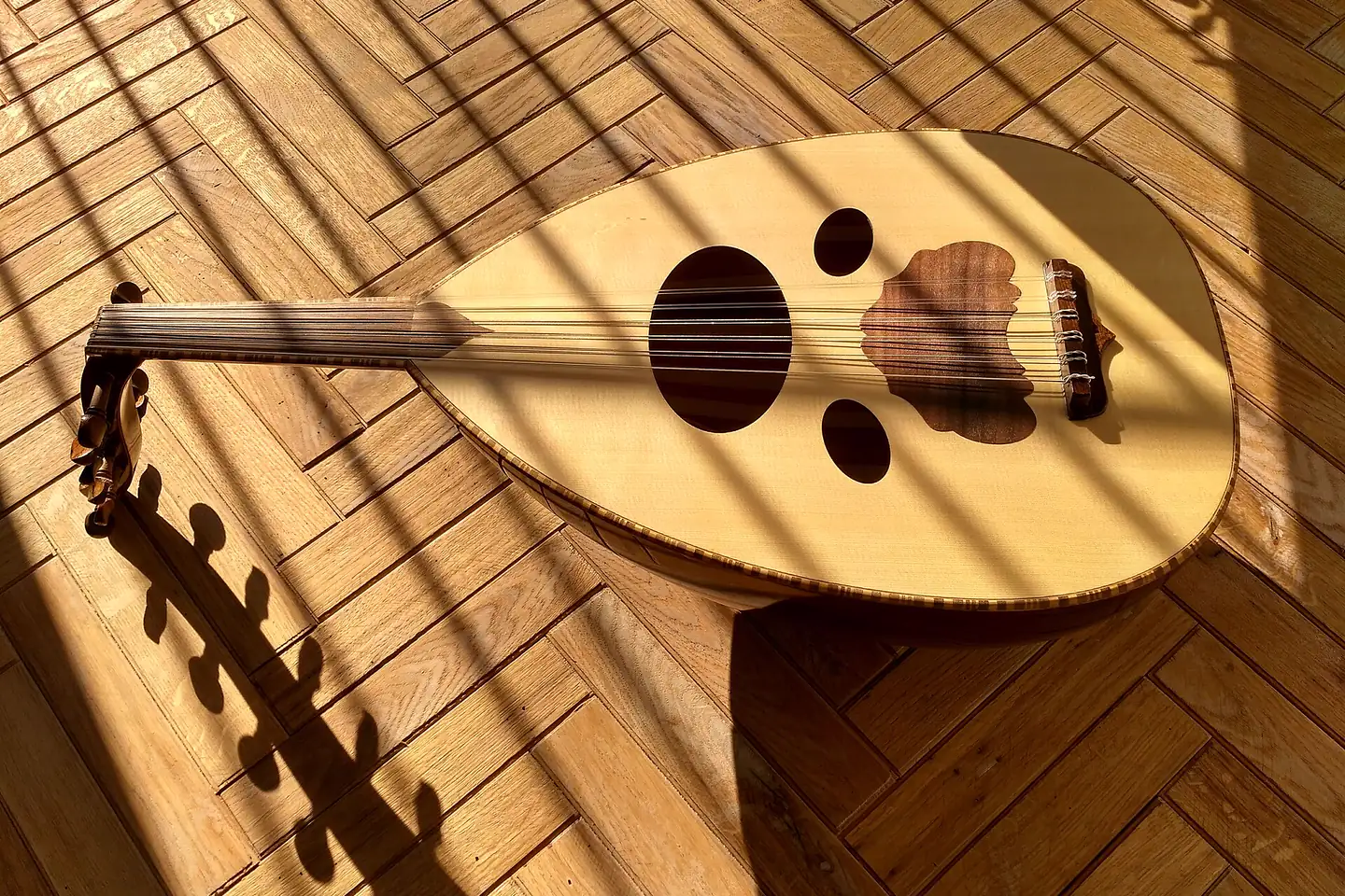 Un oud posé sur un parquet dans la lumière rasante