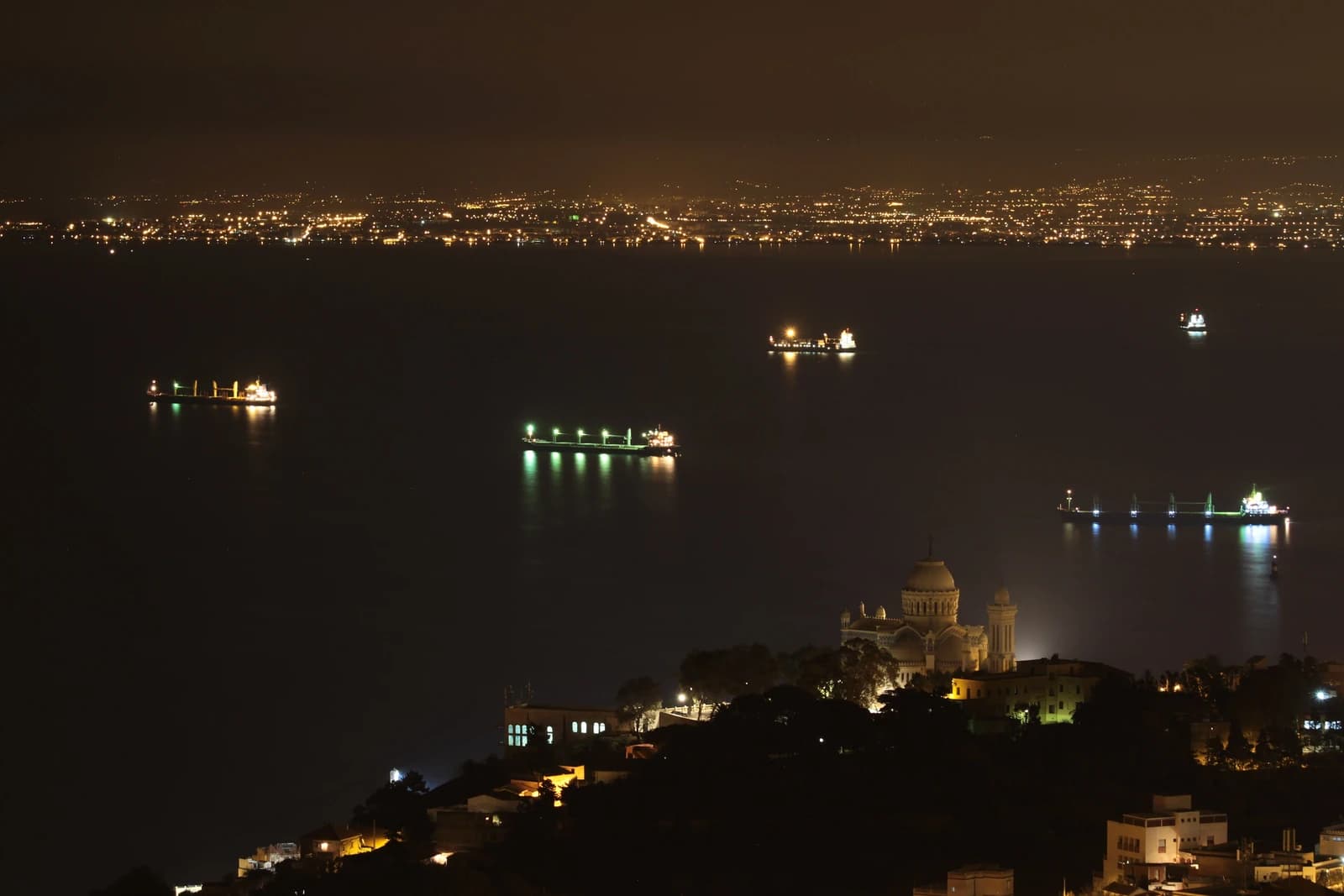 La baie d’Alger la nuit, ses navires au mouillage et Notre-Dame d’Afrique éclairée.