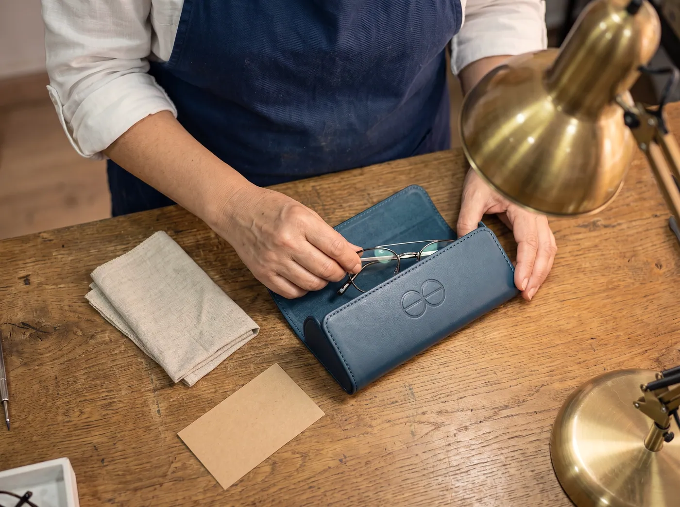 Une paire terminée rangée dans son étui bleu nuit, un chiffon de lin plié à côté