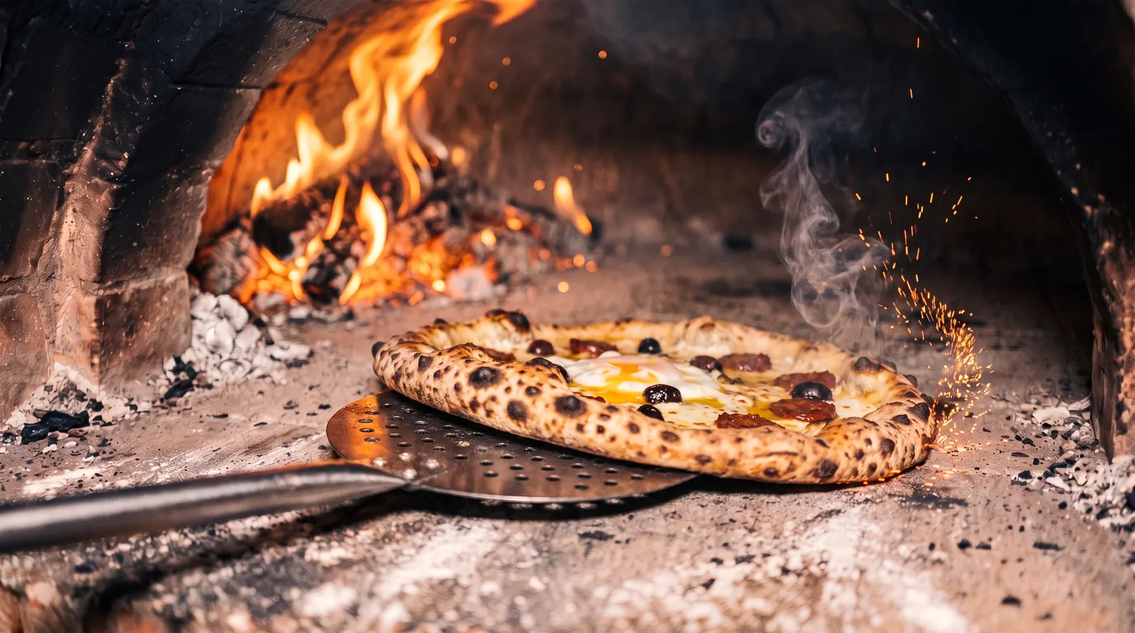 La pizza sur la pelle, à la bouche du four, au moment de la tourner