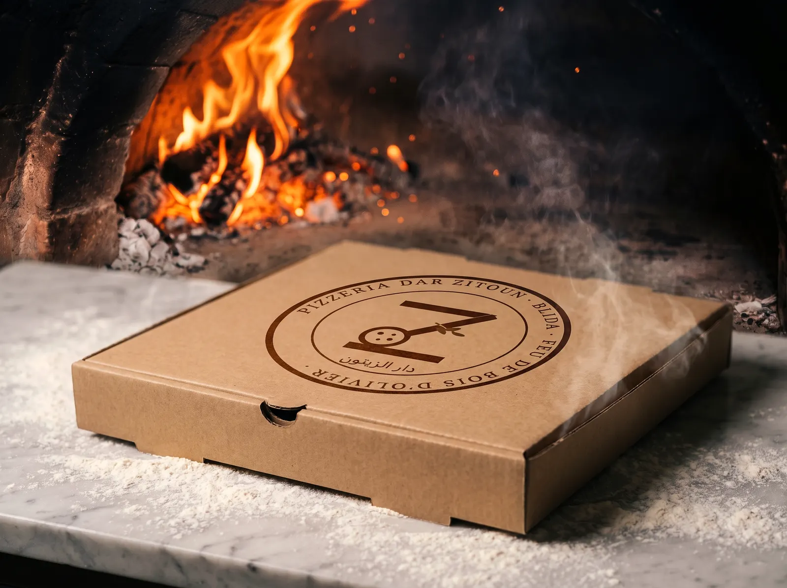 Une boîte à pizza en carton, au sceau de Dar Zitoun, posée sur le plan fariné devant le four