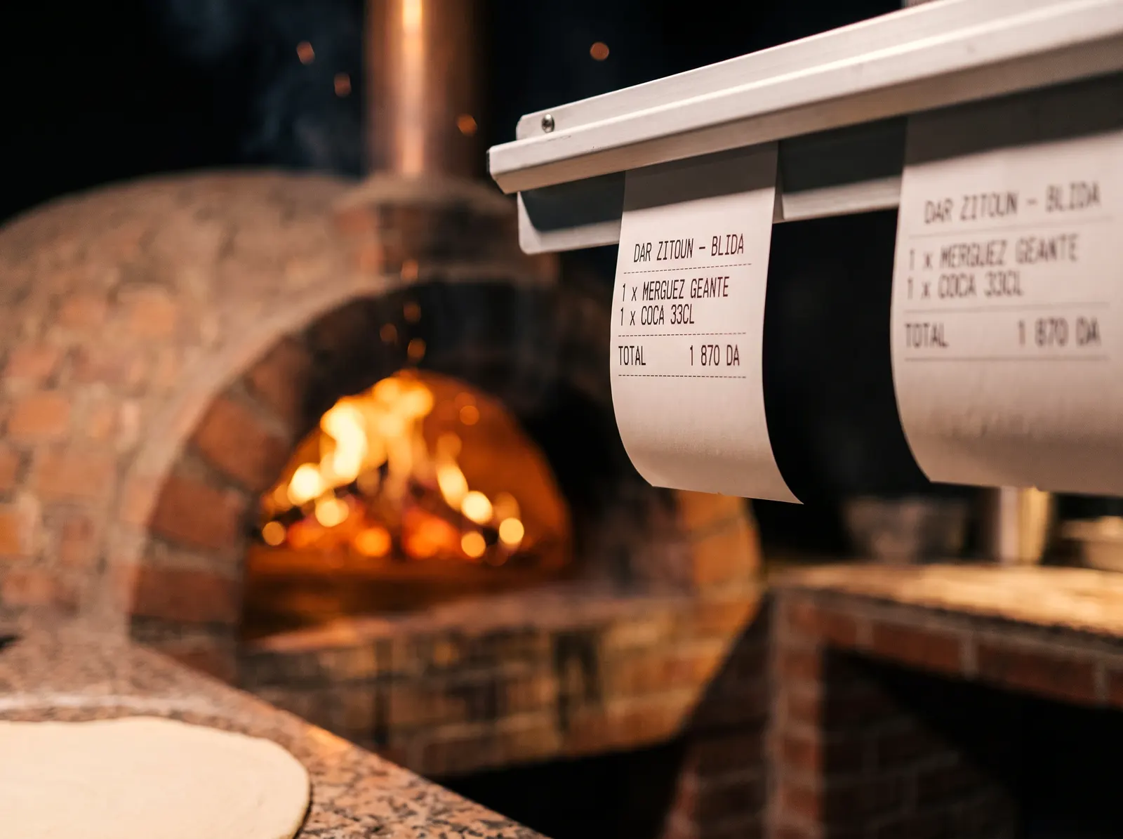 Deux tickets imprimés accrochés devant le four : une Merguez géante et un Coca